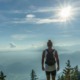 A solitary hiker with a backpack standing on a mountain peak looking out over misty valleys and layered hills under a bright sun, representing the hero's journey to the Authentic Self for highly sensitive introverts.