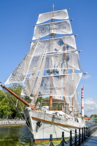 A majestic white sailing ship safely docked in a calm harbor with its large sails unfurled, illustrating the hero's journey and overcoming limiting patterns for highly sensitive introverts.