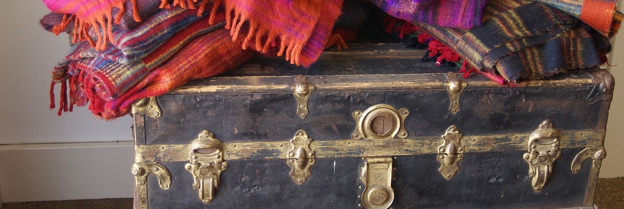 A rustic wooden chest topped with a stack of brightly colored, folded blankets, symbolizing the storage and opening of hidden emotional memories.