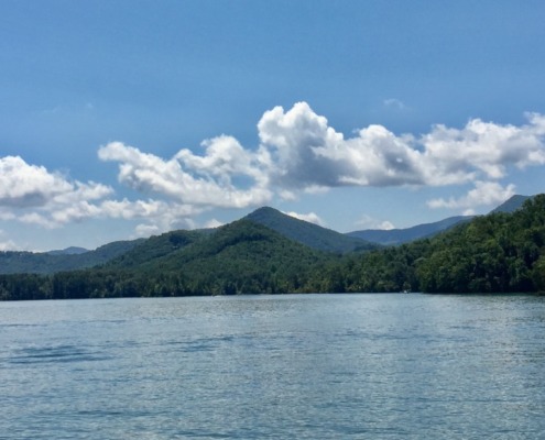 Scenic view of Lake Chatuge in Young Harris, Georgia, surrounded by green forested mountains under a bright blue sky with white clouds.