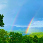 A vibrant double rainbow stretching across a wide scenic sky over a peaceful mountain landscape, symbolizing hope and transformation."
