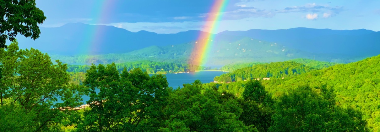 A bright rainbow spans across a dark, dramatic storm cloud sky over a lush green field.