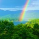 A bright rainbow spans across a dark, dramatic storm cloud sky over a lush green field.
