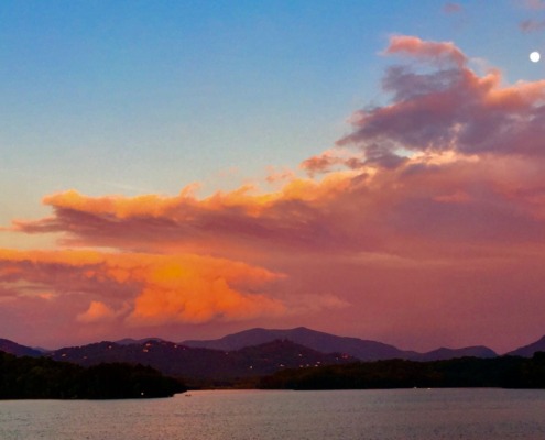 A panoramic sunset over Lake Chatuge with a full moon shining above vibrant pink and orange clouds.