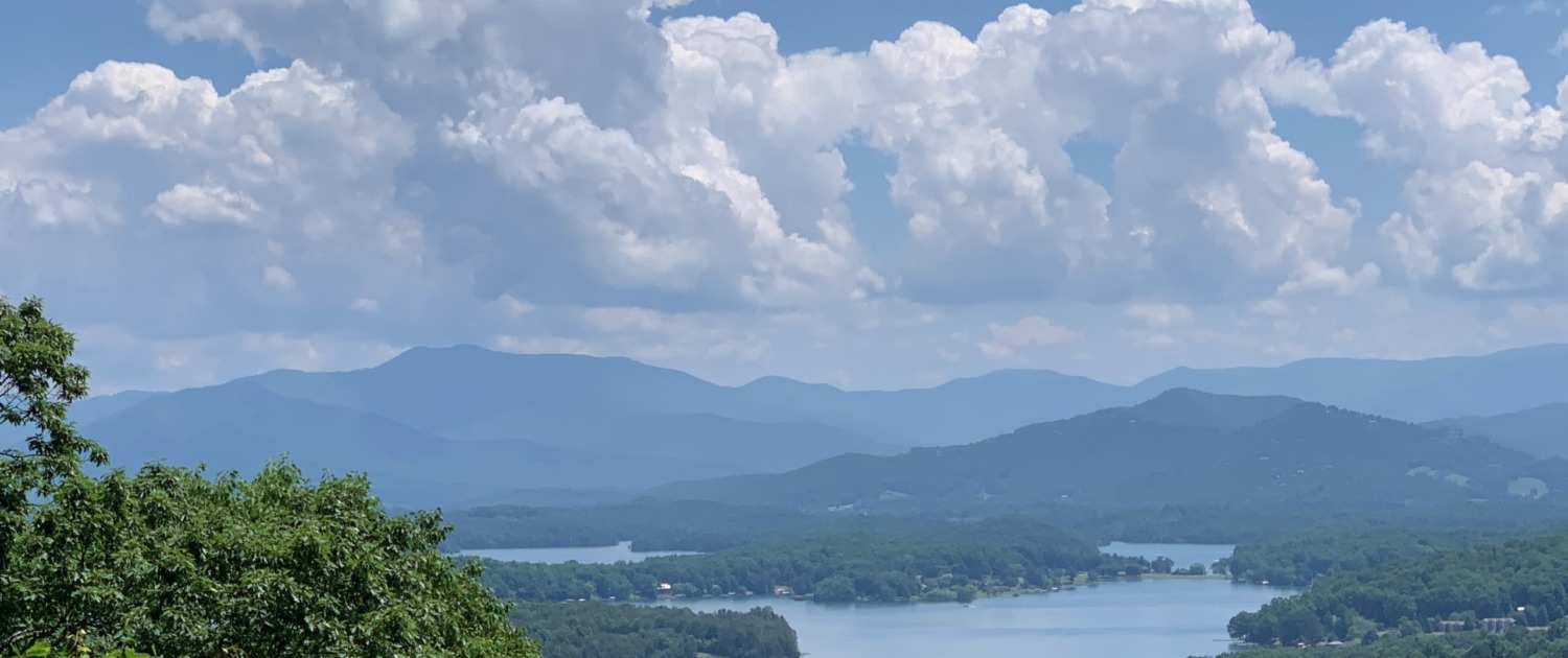 Panoramic view of Lake Chatuge and the Blue Ridge Mountains in Young Harris, GA under a bright blue sky with large white clouds.