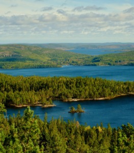 Deep blue lake inlets, heavily forested green hillsides, and tree-covered islands under a partly cloudy sky.