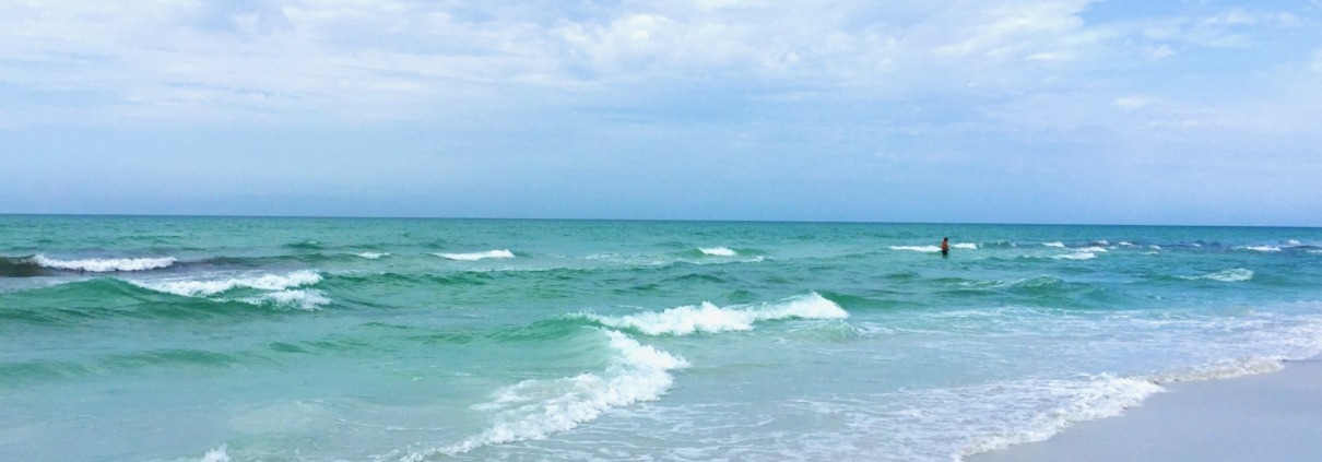 A peaceful beach scene on the Florida Gulf Coast featuring turquoise water with gentle waves lapping onto soft white sand under a bright sky with soft clouds, capturing the restoring essence of an HSP Breathwork Retreat with Benita Esposito.