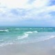 A peaceful beach scene on the Florida Gulf Coast featuring turquoise water with gentle waves lapping onto soft white sand under a bright sky with soft clouds, capturing the restoring essence of an HSP Breathwork Retreat with Benita Esposito.