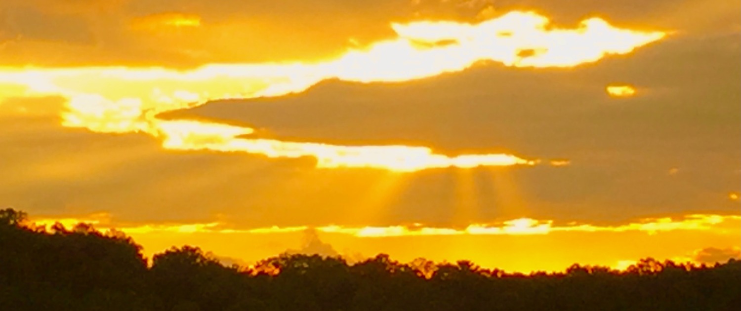 Golden sunbeams breaking through thick clouds over a dark mountain treeline in Young Harris, Georgia.
