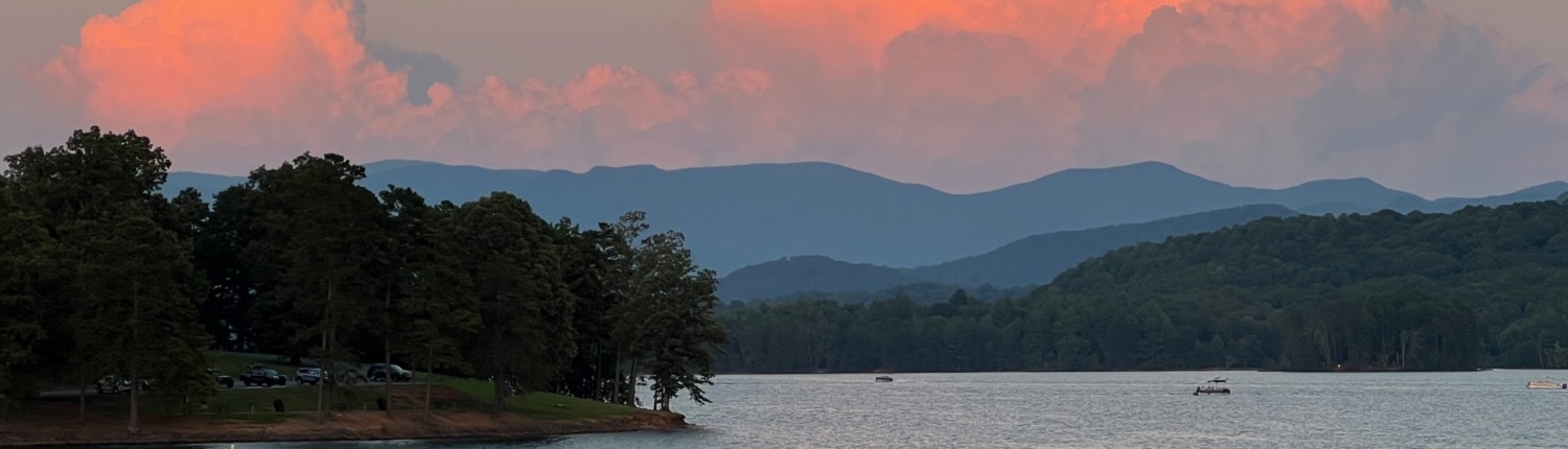 The calm waters of Lake Chatuge reflecting a pastel sunset sky over the Blue Ridge Mountains, serving as a peaceful backdrop for an HSP Breathwork Retreat in Young Harris, Georgia, with Benita A. Esposito, LPC
