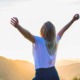 A woman stands at a mountain summit with arms raised wide during a sunset over the North Georgia Mountains. This captures the triumphant "mountain top" breakthrough experience of an HSP Breathwork Retreat with Benita Esposito.