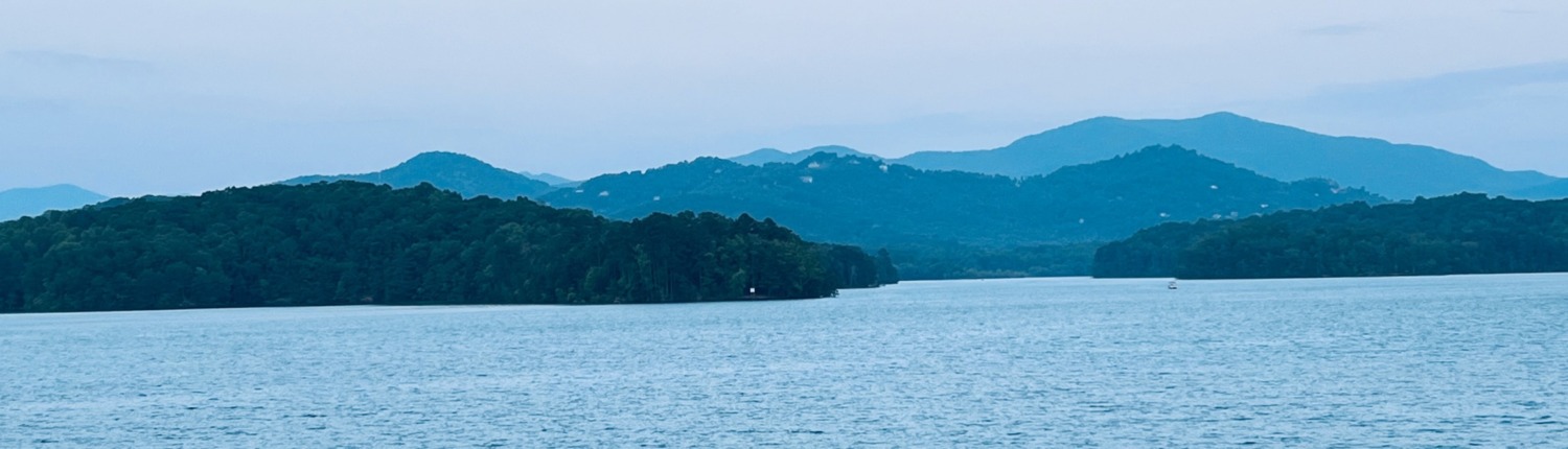 Peaceful blue mountain lake surrounded by lush green forests and rolling layers of mountain peaks after a Highly Sensitive Person (HSP) Retreat.