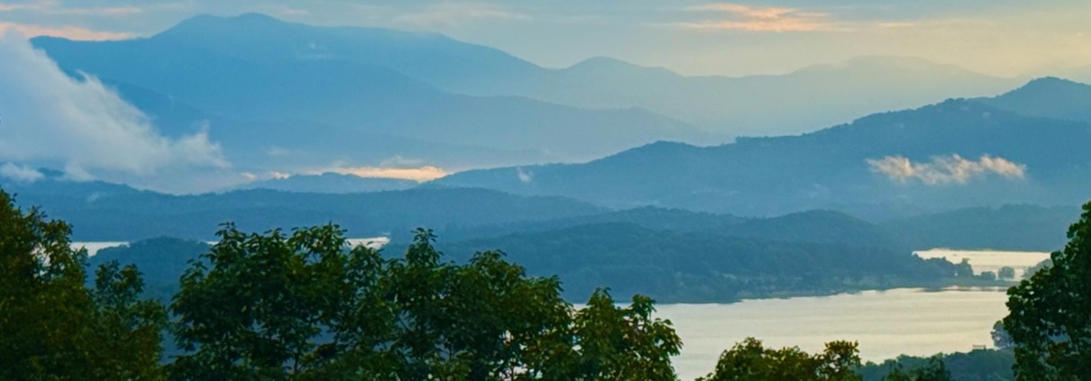 A scenic, peaceful view of the misty Blue Ridge Mountains and Lake Chatuge at dawn, captured by Benita A. Esposito to evoke emotional healing, calmness, and stillness for highly sensitive introverts.